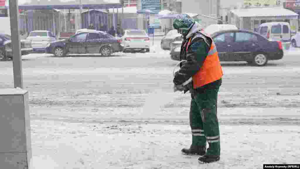 Дворник посыпает реагентом тротуар на автобусной остановке на улице Киевской