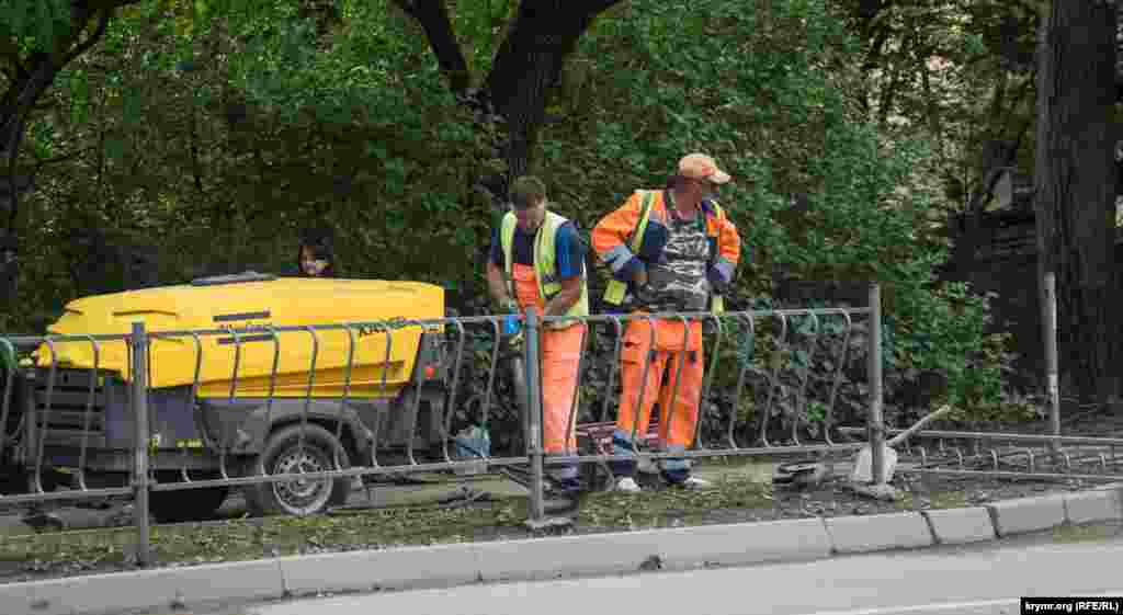 С помощью отбойного молотка демонтируется железный заборчик у сквера Мира